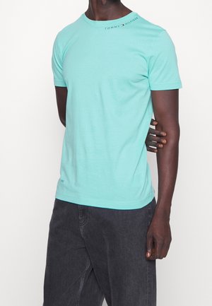 Krótki rękaw t-shirt w jasnym turkusowym kolorze z okrągłym dekoltem i małym logo na ramieniu. W zestawieniu z ciemnymi dżinsami. Gładka bawełniana faktura.