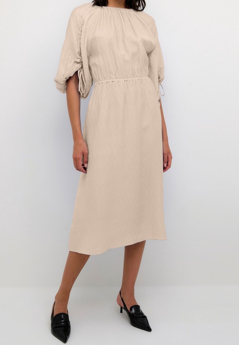 Beige midi mekko, jossa on pystysuora raidoitus, joustavat pallohihojen, vyötärö on kireällä ja se on yhdistetty mustiin kärjellisiin korkokenkiin.