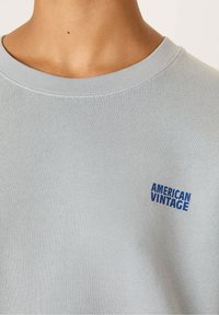 Felpa azzurra realizzata in morbido tessuto con colletto a coste. Presenta un piccolo logo blu "AMERICAN VINTAGE" sul davanti.