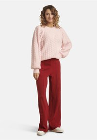 Light pink textured pullover with puffed sleeves paired with high-waisted red wide-leg pants; model wears white sneakers.