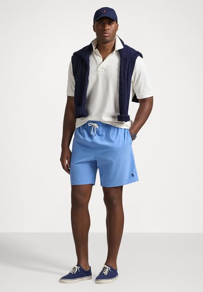 Căciulă marină, tricou polo alb, vestă tricotată bleumarin, pantaloni scurți albaștri deschiși și adidași albaștri. Logo-ul notabil cu ponei pe pantaloni scurți, talie cu șnur.