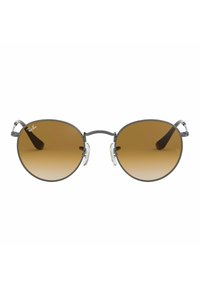 Occhiali da sole rotondi, con tonalità marroni, dotati di una sottile montatura in metallo grigio, naselli trasparenti e punte delle aste in acetato marrone. Logo Ray-Ban sulla montatura.