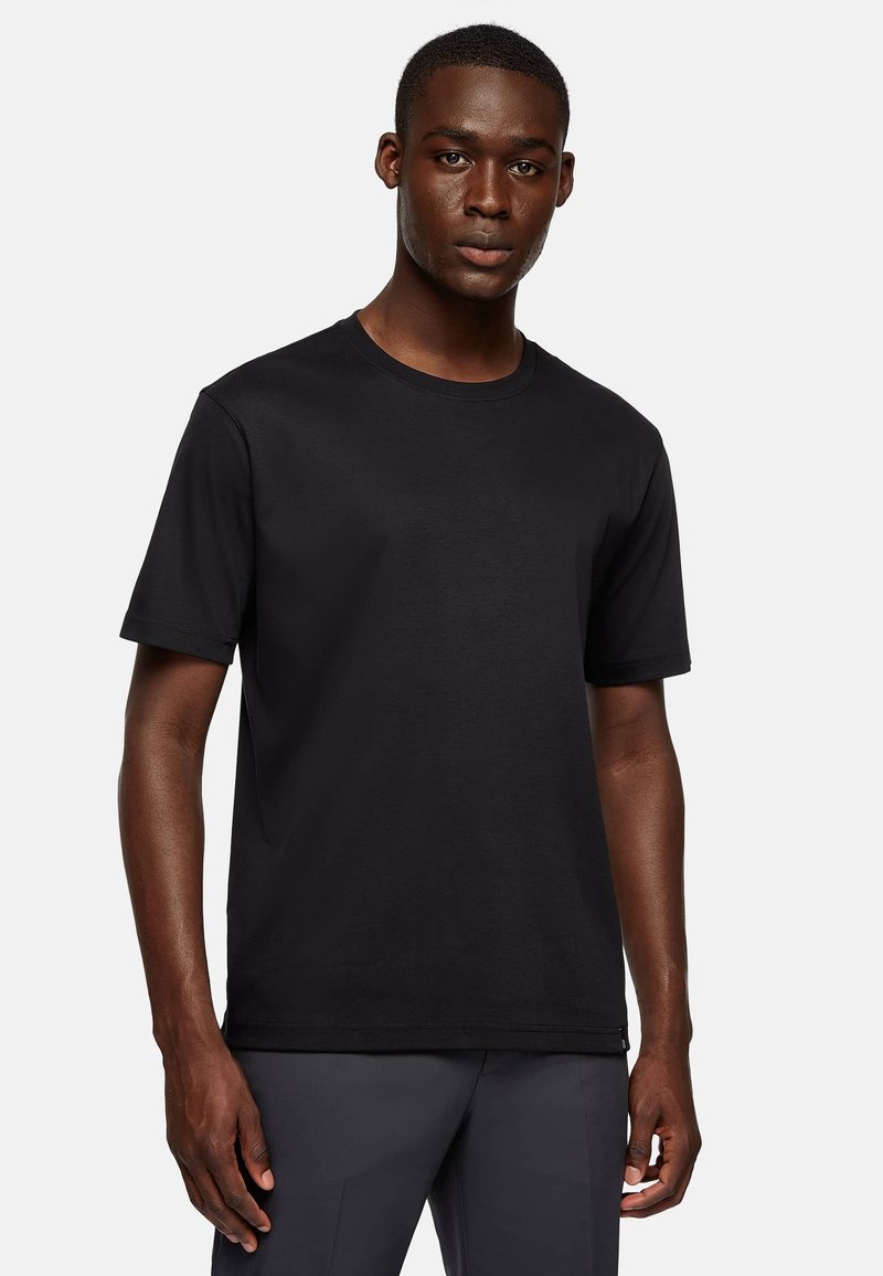 Black short-sleeve t-shirt made of cotton. Classic crew neck design with a smooth texture. Model wears it with dark trousers.