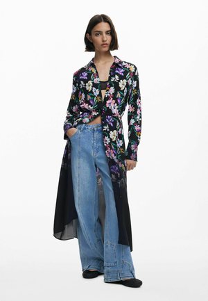 Bluse mit floralem Muster in Schwarz, mit langen Ärmeln und einem Bindeband-Design. Kombiniert mit weit geschnittenen Jeans aus Denim, hell gewaschen und mit Taschen.