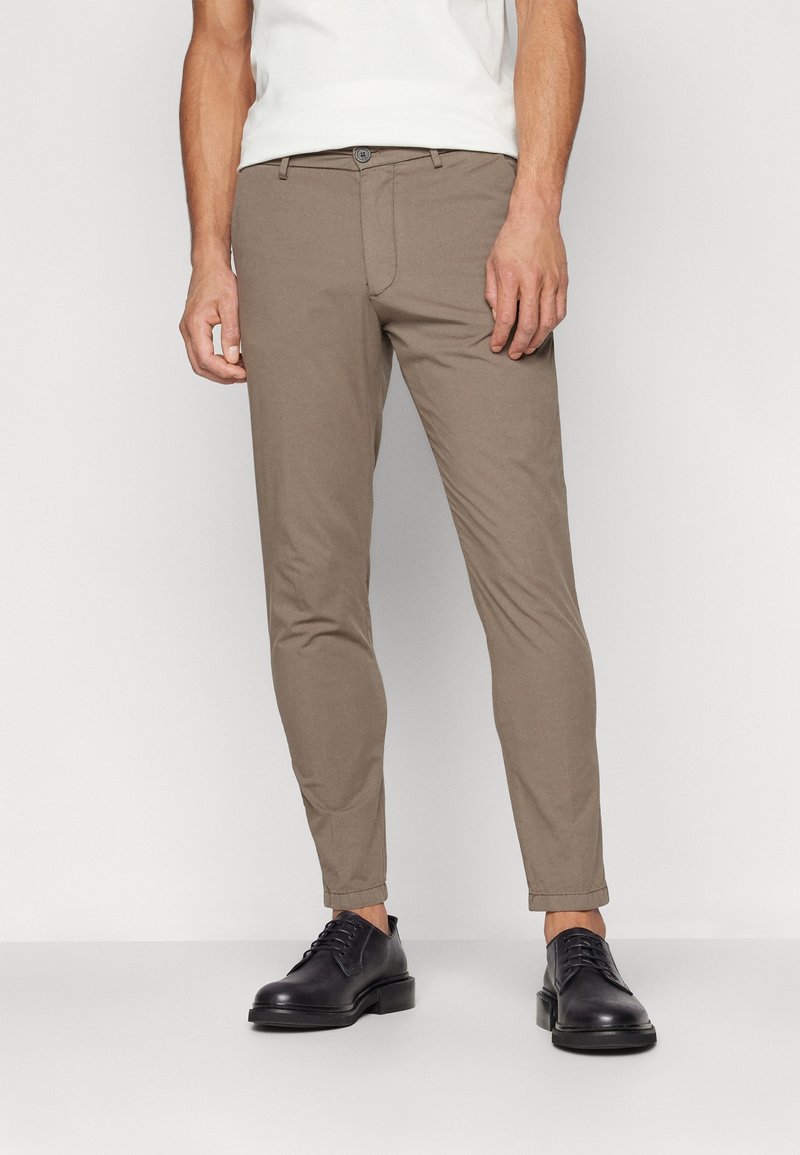 Ljusbruna chinos med smal passform, med knappstängning, sidofickor och en mjuk textur, kombinerade med svarta snörskor.