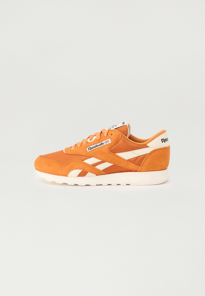 Oransje mockask sneaks med hvite detaljer, som har et klassisk design, snøring foran og en strukturert gummisåle. Reebok-merke på tungen.