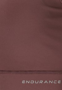 Bordeaux sporttanktop gemaakt van een gladde, rekbare stof met een zilveren logo onderaan en platte naden voor comfort.
