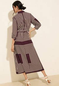 Langes, fließendes Kleid in tiefem Burgunderrot mit kontrastierenden breiten cremefarbenen geometrischen Streifen. Es hat einen Gürtel in der Taille und Dreiviertelärmel.