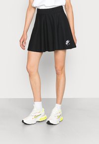 Svart utsvängd kjol med resårmidja och en vit Nike Air-logotyp. Matchas med vita och neongula träningsskor och ankelsockor.