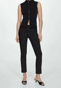 Czarny bezrękawnik zapinany na zamek i dopasowane czarne spodnie, oba wykonane z gładkiego materiału, z krótkim krojem i minimalistycznymi detalami.