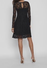 Black lace dress with long sleeves, floral pattern, keyhole back detail, and flared skirt. Lined bodice and scalloped hem.