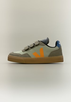Χαμηλό sneaker με πάνω μέρος από μπεζ καστόρι και δέρμα, πορτοκαλί λογότυπο "V", τρεις ιμάντες με βέλκρο, σόλα από καουτσούκ και μπλε ταμπελάκι στη φτέρνα.