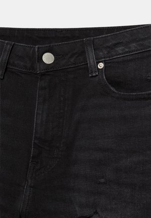 Czarne jeansy z denimu - zbliżenie pokazujące pas, guzik, szlufki na pasek, przednią kieszeń oraz subtelne przetarcia na materiale.