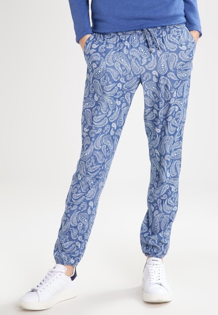Pantalons à motif paisley bleu en tissu léger, dotés d'une taille élastique et de poignets, associés à des baskets blanches.