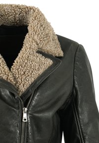 Giacca in pelle nera con colletto in sherpa beige, chiusura con zip frontale e tessuto testurizzato, caratterizzata da un design elegante e aderente.