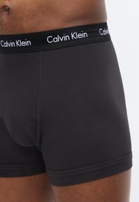 Záber zblízka na osobu nosiacu čierne boxerky Calvin Klein s pásom so značkou.