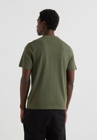T-shirt vert olive à manches courtes fabriqué en coton doux, avec un col rond et une texture lisse et uniforme. Design minimaliste sans logos visibles.