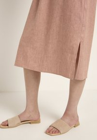 Ein knielanges, pinkes Leinenkleid mit einem seitlichen Schlitz, kombiniert mit beigen Wildleder-Sandalen mit flacher Holzsohle.