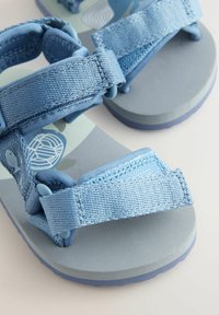 Ljusblå sandaler med textilremmar, justerbara stängningar och vadderade sulor som har en minimalistisk design och subtila mönster.
