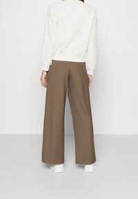 Sudadera blanca con puños y dobladillo acanalados que se combina con pantalones de pierna ancha marrones. Los pantalones tienen una textura suave y son de longitud hasta el tobillo. Zapatillas blancas completan el look.