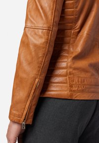 Bruine leren jas met een gestructureerde afwerking, horizontale stikdetails en een ritssluiting bij de mouwen. Slank ontwerp.