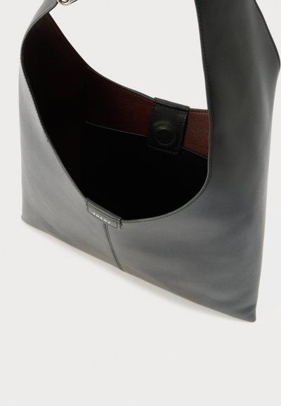 Sac à épaule en cuir noir avec une large bandoulière, ouverture supérieure, fermeture à pression magnétique, et détail de couture avec logo sur le devant.