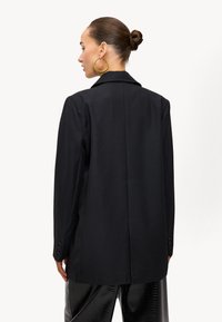 Zwarte op maat gemaakte blazer met een geknipte kraag, enkele knoopsluiting en gestructureerde schouders. Gladde textuur, rechte snit en mouwen met vier knopen.