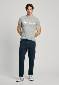 Grå bomulds t-shirt med "Pepe Jeans London" logo i hvid, sammen med marineblå cargo-bukser. Skoene er hvide med grå detaljer.