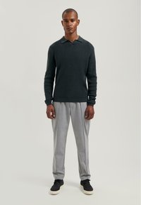 Dark green knit sweater with a collared neckline, paired with light gray pleated pants and black sneakers. Textured fabric and relaxed fit.