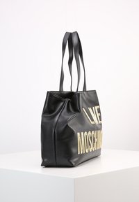 Černá kožená taška přes rameno s pozlaceným embosovaným textem "LOVE MOSCHINO", strukturovaný tvar, dvě dlouhé uši a texturovaný povrch.