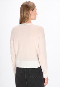 Vaaleanbeige viltti, joka on valmistettu pehmeästä materiaalista, ja siinä on ribboribattu helma ja hihansuut, pyöreä kaula-aukko sekä huomaamaton logo-yksityiskohta takana.