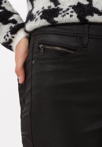 Pantalones negros con un bolsillo lateral con cremallera metálica, textura suave y detalle de costura a lo largo del lado.