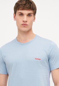 Light blue cotton t-shirt with a crew neck and short sleeves, featuring a red "HUGO" logo on the left side of the chest.