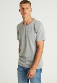 Grijze katoenen t-shirt met korte mouwen, ronde hals en een klein rechthoekig logo op de borst. Draag het met blauwe spijkerbroek.