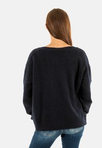 Maglione oversize blu navy con vestibilità morbida e tessuto testurizzato, caratterizzato da un ampia scollatura e spalle cadenti, abbinato a jeans blu.