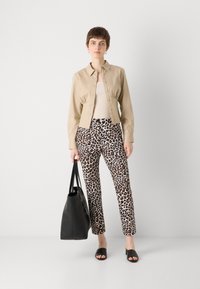 Chemise cropped beige à boutons, débardeur clair, pantalon imprimé léopard, sandales noires, et un grand sac fourre-tout noir. Texture de tissu lisse.