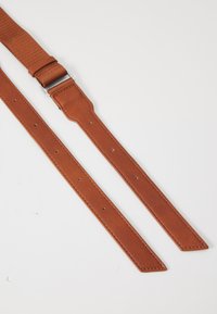 Cinturino in pelle marrone con una finitura testurizzata, dotato di una fibbia in metallo e fori per la regolazione. Il design è allungato e piatto, con estremità appuntite.