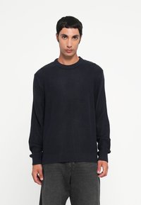 Pull en maille bleu marine avec un col rond et des manches longues ; présente un motif texturé et des bords-côtes aux poignets et à l'ourlet.
