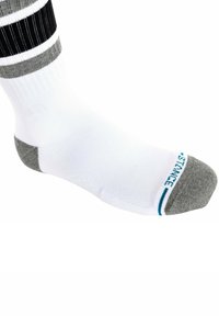 Calzino sportivo bianco con tallone e punta grigi, dotato di strisce nere e grigie nella parte superiore e il logo blu "STANCE" di lato.