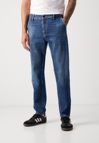 Blugi din denim albastru cu o croială dreaptă, design cu cinci buzunare și o ușoară decolorare. Purtați cu pantofi negri cu dungi albe.