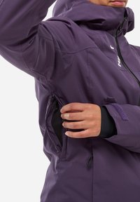 Person wearing a purple jacket opening a zippered underarm ventilation vent, showing black mesh lining inside.