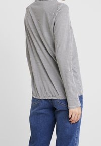 Langärmliges Hemd im schwarz-weißen Hahnentupfmuster, entspannte Passform, strukturierter Stoff, runder Ausschnitt, kombiniert mit blauen Jeans.