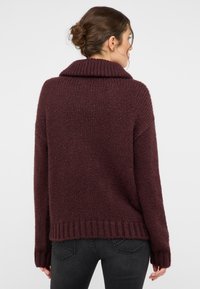 Burgunderfarbener Strickpullover mit hohem Kragen, lockerer Passform, geripptem Saum und langen Ärmeln, der aus einem weichen, strukturierten Stoff gefertigt ist.