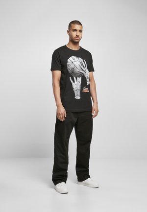 Schwarzes Baumwoll-T-Shirt mit einem Grafikmotiv von Händen, die einen zerbrochenen Basketball halten, und dem Text "Lasts Forever" in Orange, kombiniert mit schwarzen Hosen.