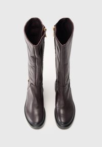 Bottes en cuir brun hauteur genoux avec une texture lisse, bout arrondi et fermetures éclair sur le côté. La couleur est uniforme avec un éclat subtil.