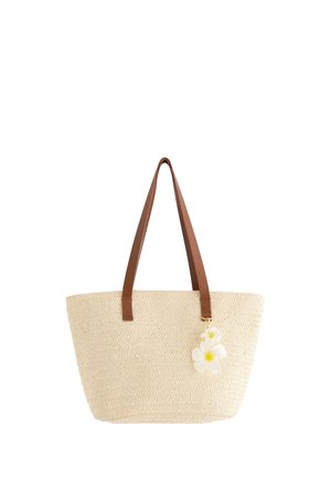 Beige vævet mulepose med lange brune håndtag og to hvide blomster med gule centre, der er fastgjort som dekoration.