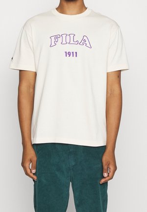 Kreemipaita, millel on lillakas "FILA" logo ja 1911 detail. Lühikesed varrukad, ümmargune kaelus, sile tekstuur. Kombineeritud türkiissiniste sametpükstega.