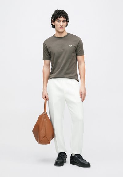 Khaki tričko s krátkymi rukávmi a malým logom, doplnené o biele upravené nohavice. Hnedá kožená taška, čierne tenisky s textúrou.