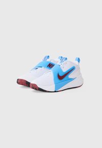 White athletic shoes with a blue overlay, featuring a red Nike logo and accents. Textured fabric with a rubber sole and heel tab.