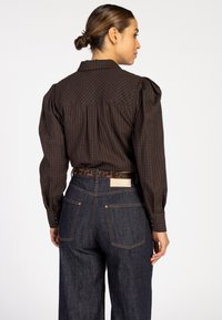 Bruine geruite shirt met pofmouwen, knoopmanchetten en een achterpand, gecombineerd met donkere denim jeans en een riem met luipaardprint.